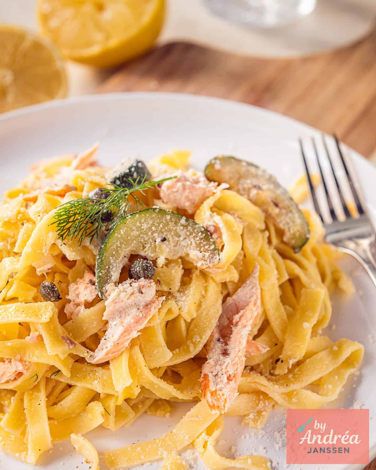 A white plate with tagliatelle, zucchini, salmon and a creamy sauce.