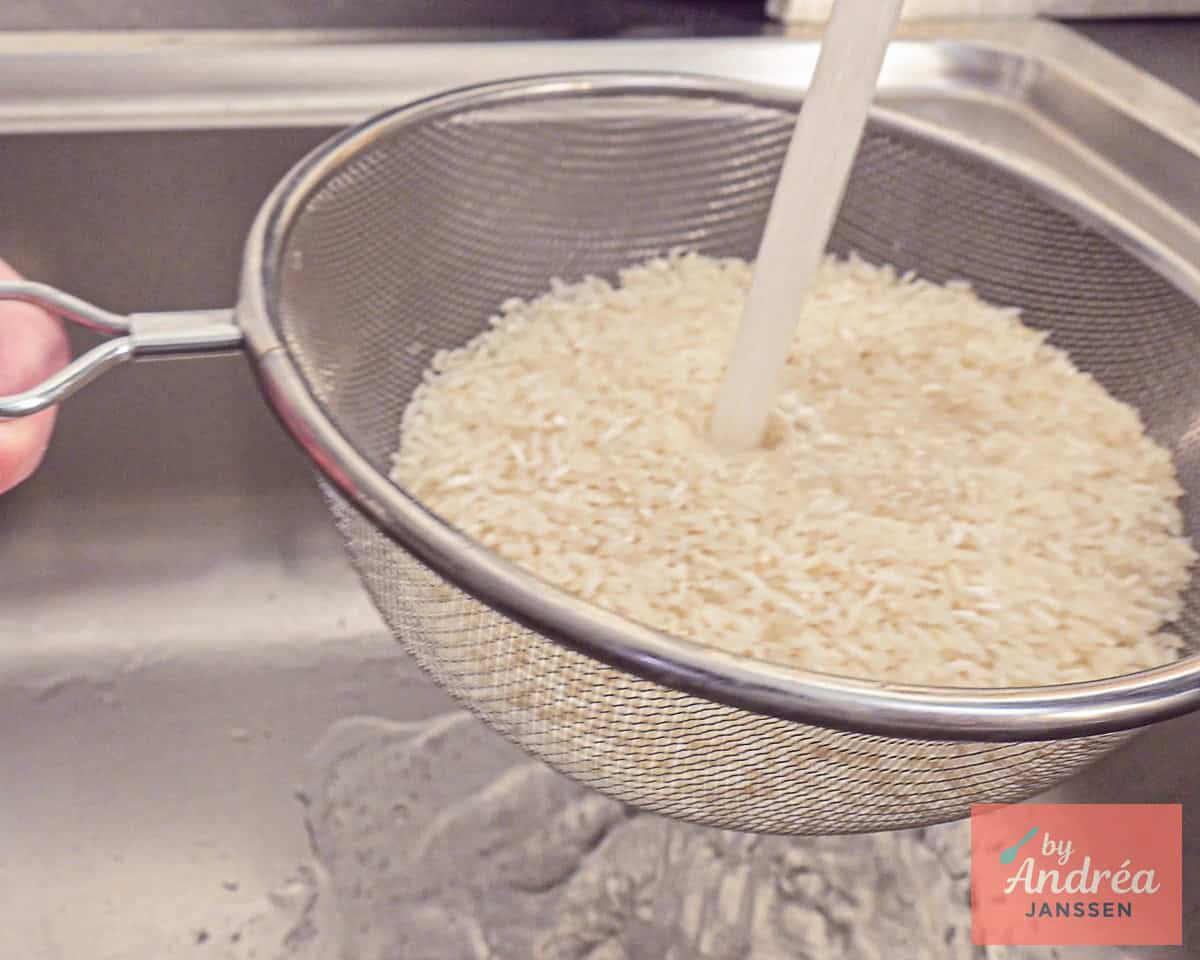 Long grain rice is rinsed under the tap.