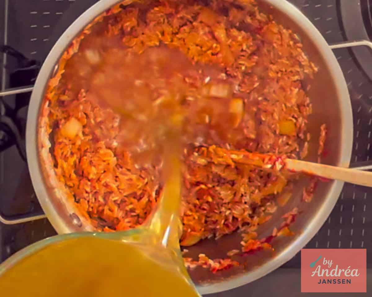 The broth is poured into the pan with the red rice.