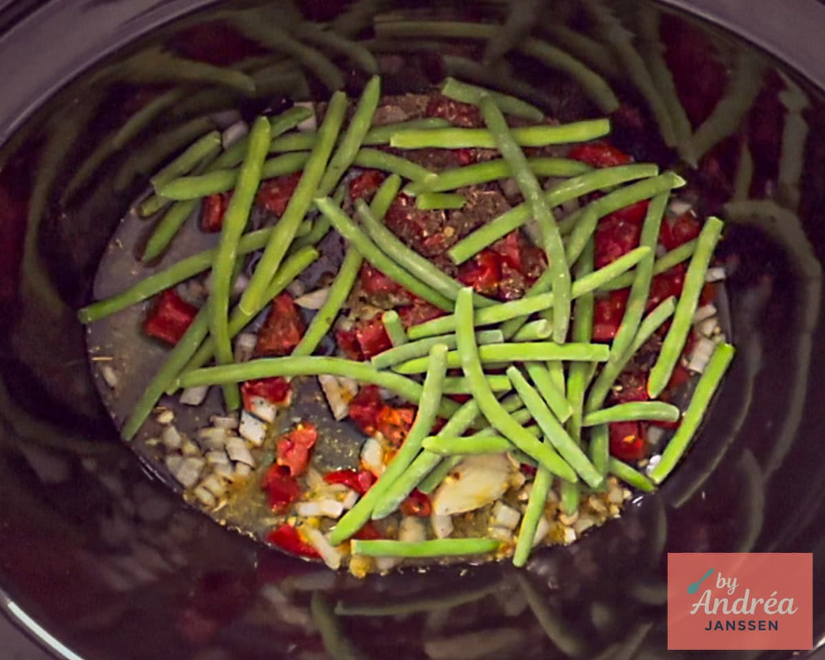 Slowcooker filled with onion, tomatoes, garlic, cream and green beans