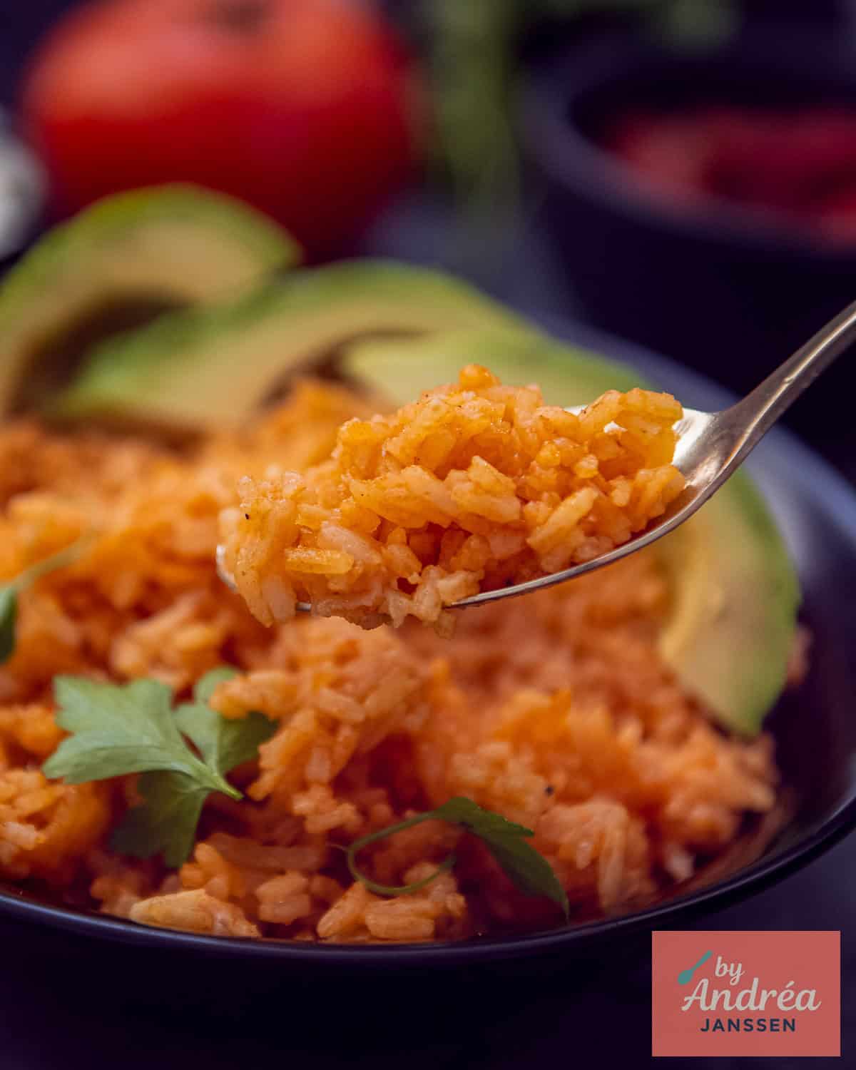 A bowl of Mexican rice with tomato and herbs. A spoonful takes a scoop.