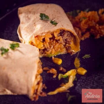 A square photo of a cut-open burrito with a filling of rice, corn, ground beef, cheese, cabbage, tomato, and onion.