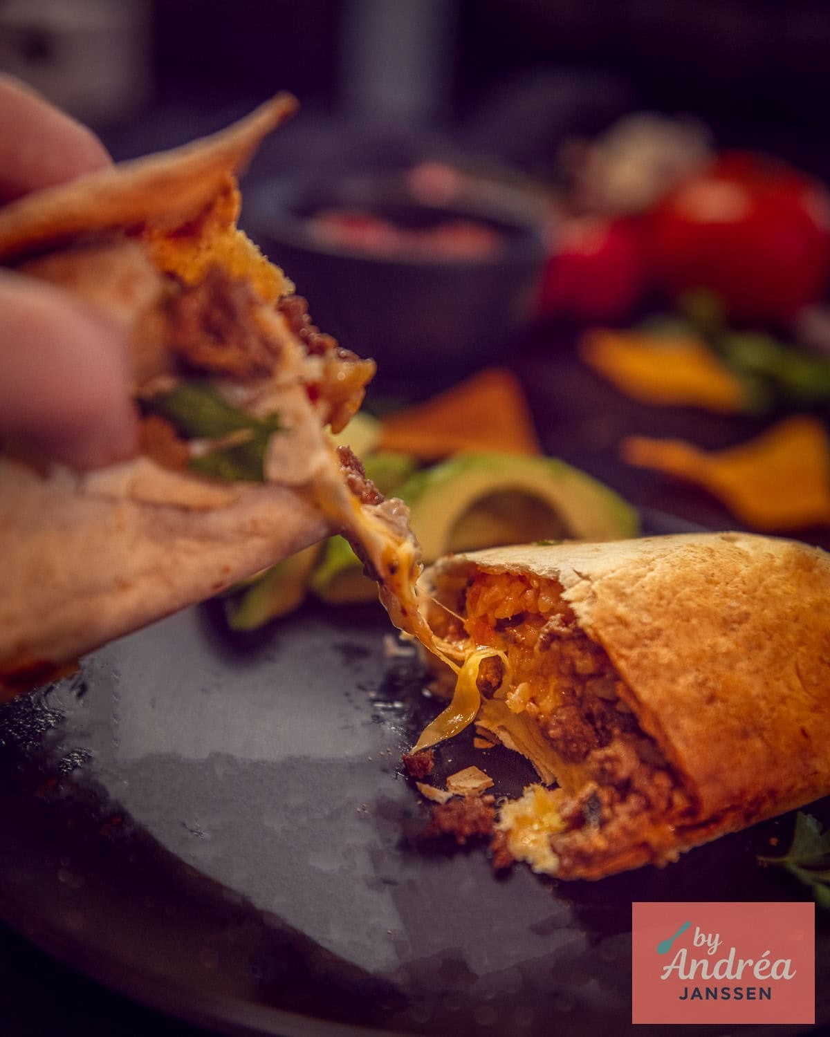 Two halves of a burrito filled with minced meat and rice being pulled apart. A cheesy string is visible.