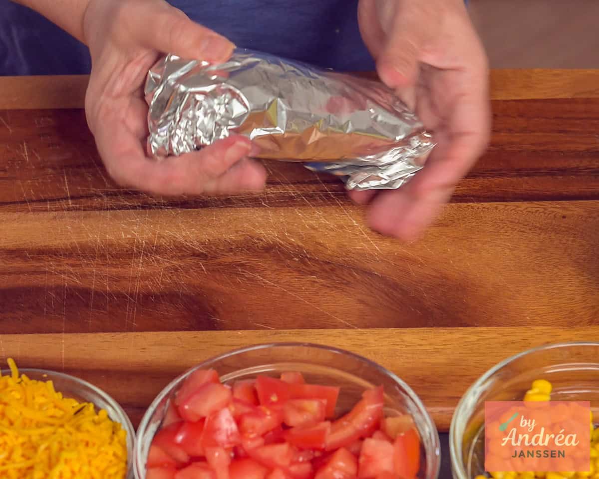 The burrito folded in foil, all the ingredients for the filling are in the foreground.