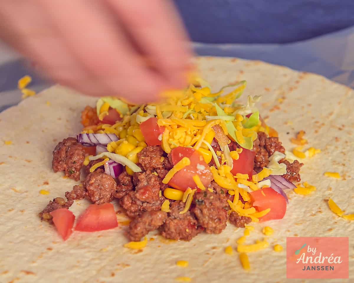 A wrap topped with a filling of minced meat, tomato, cabbage, corn, onion, and cheese.