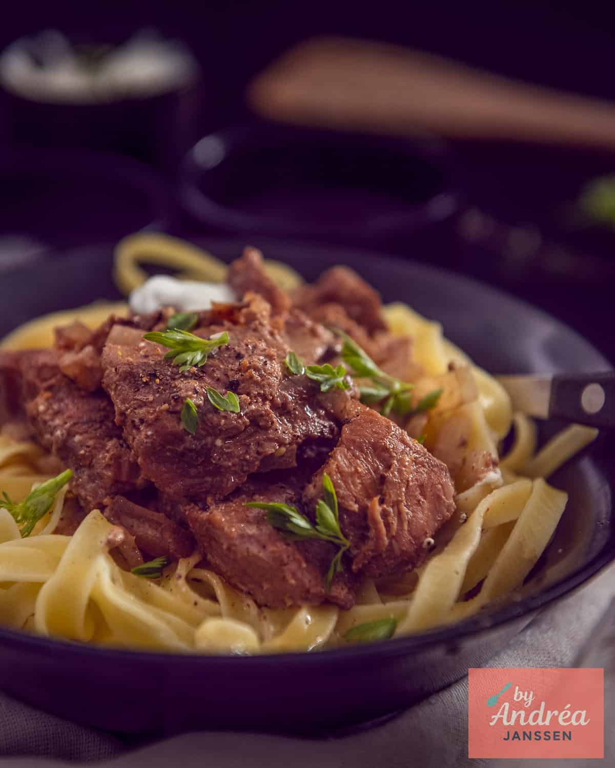 A small black dish with tagliatelle and stroganoff.