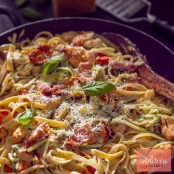 A square photo of a sauté pan with pasta, chicken, and creamy sauce with bacon.