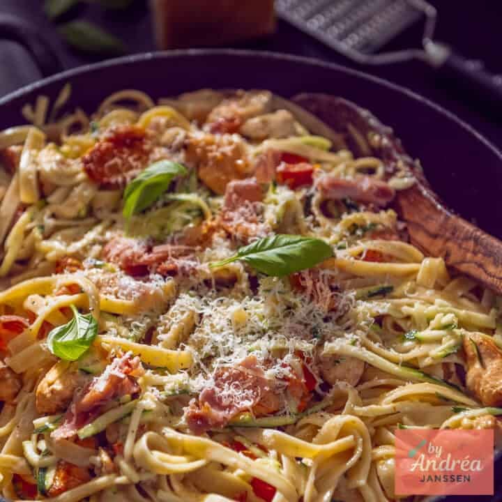 A square photo of a sauté pan with pasta, chicken, and creamy sauce with bacon.