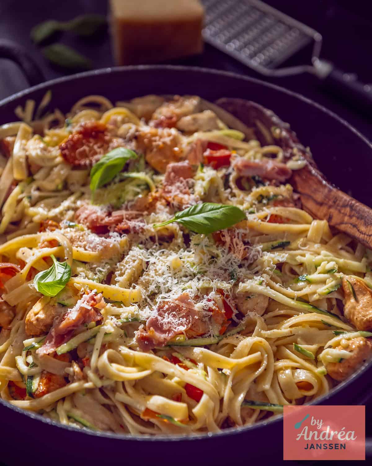 Part of a casserole filled with fettuccine pasta with a creamy sauce with bacon, sun-dried tomatoes, and bacon.