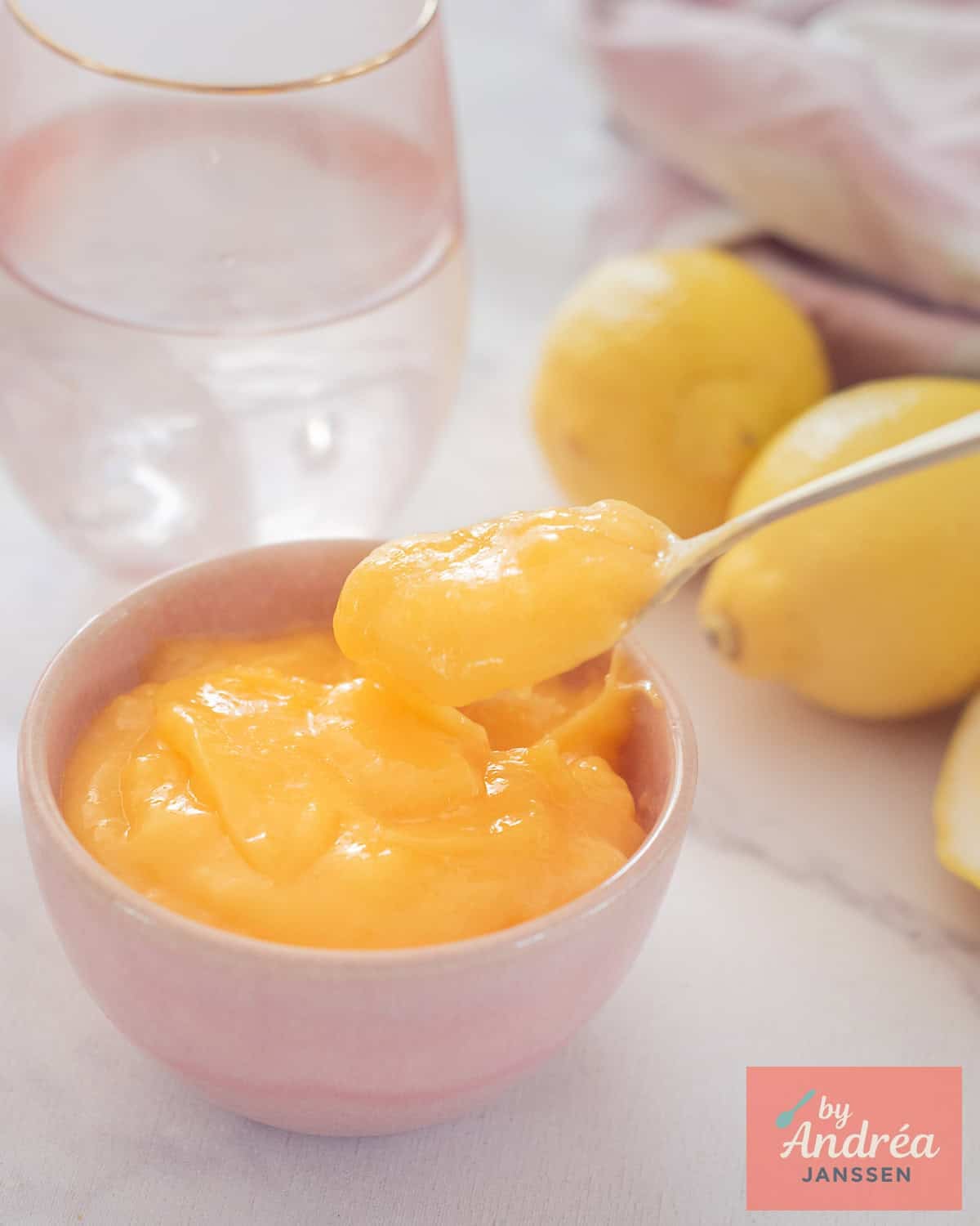 A pink bowl of lemon curd, a spoon takes a scoop out of it.