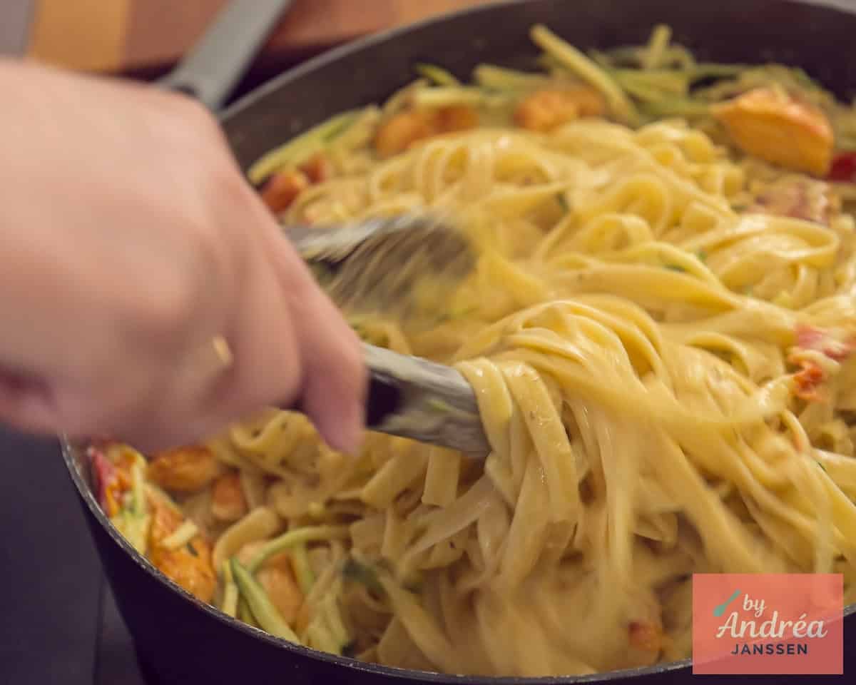 A sauté pan with pasta with chicken, creamy sauce, and bacon that is tossed together