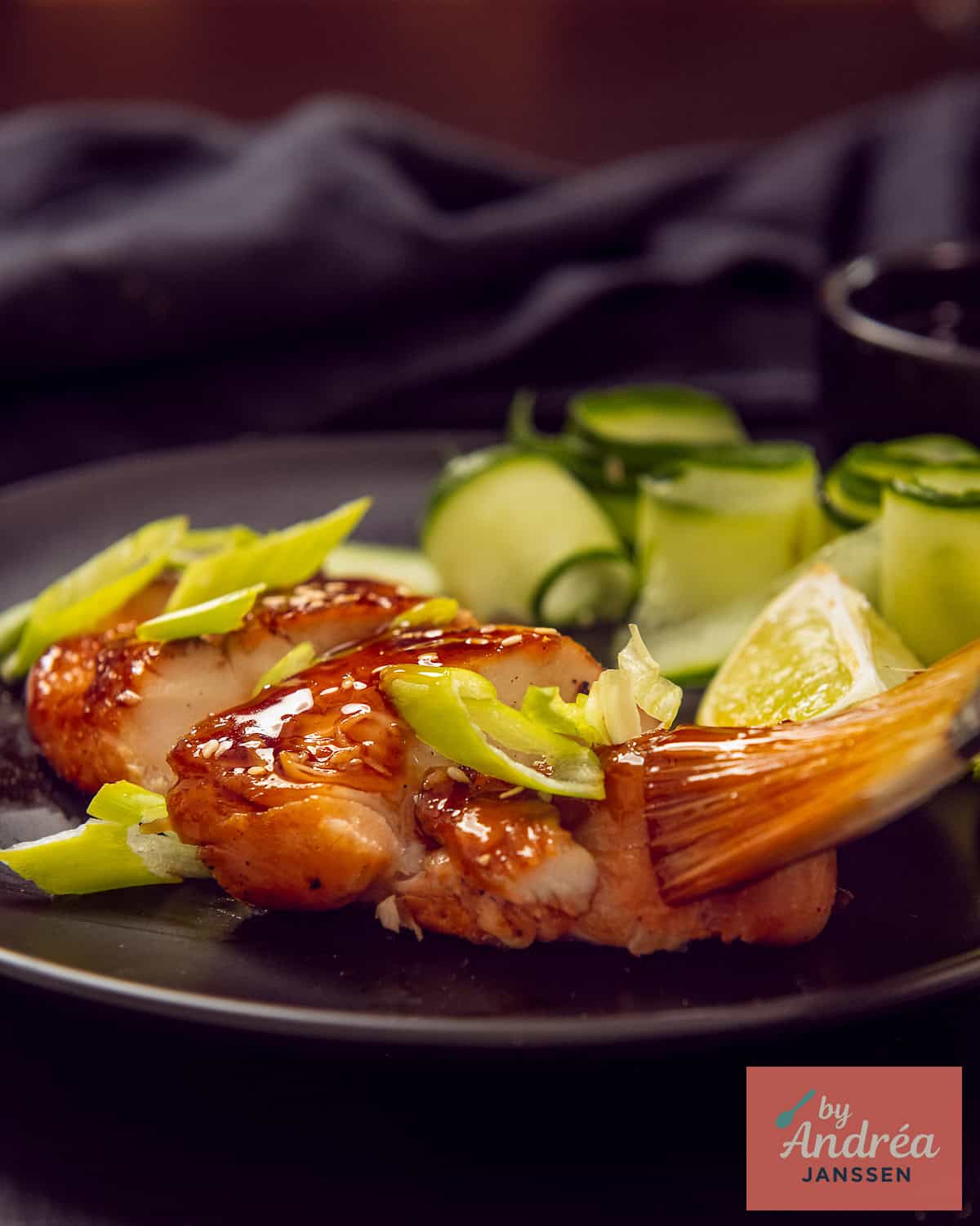 A brush spreads some sauce over the slices of chicken lying on a black plate.