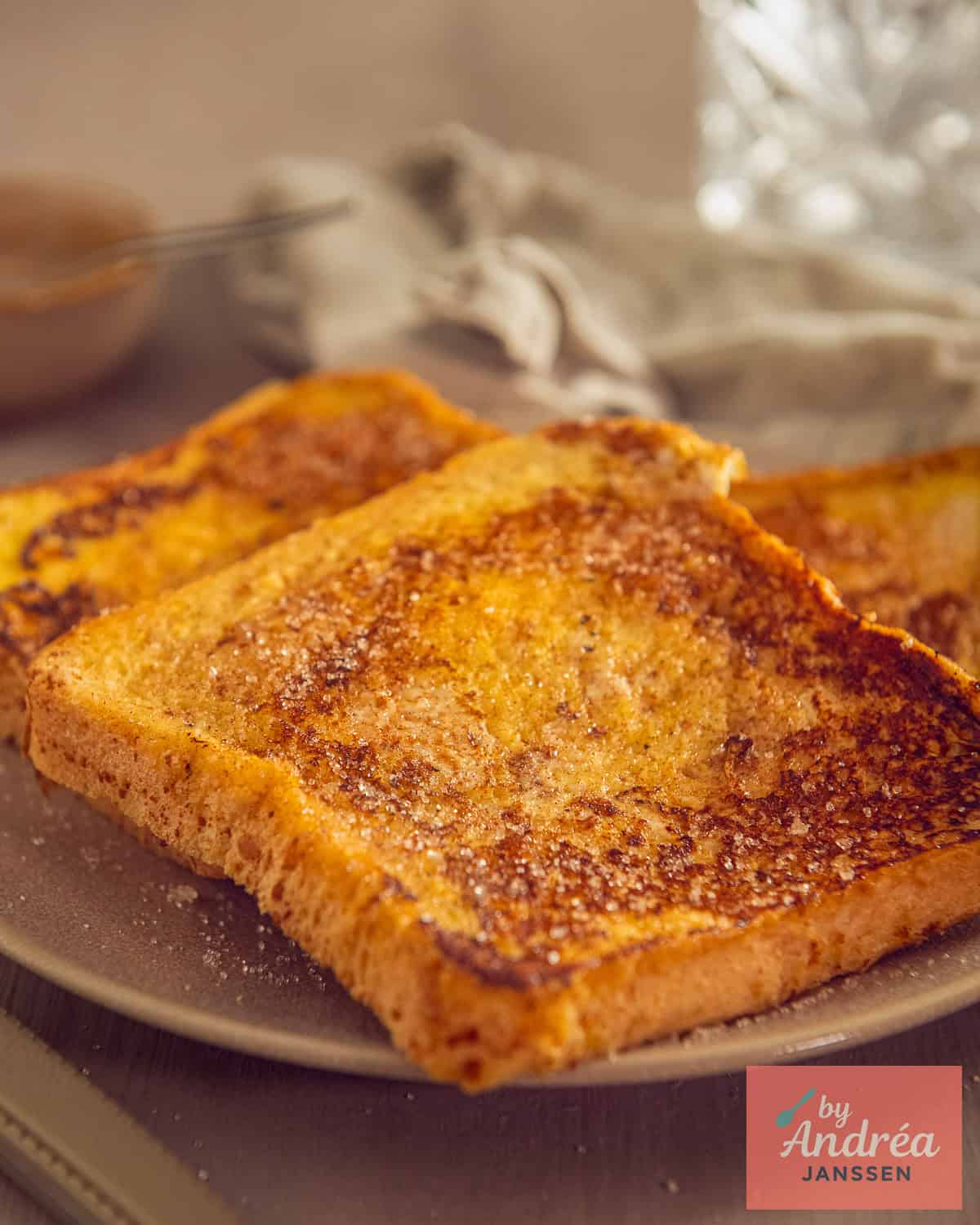 Three French toast slices on a taupe plate sprinkled with sugar.