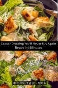 Close-up of Caesar salad in a dark bowl with golden crispy croutons, shaved Parmesan cheese and creamy dressing over fresh romaine lettuce, with a fork resting in the bowl.