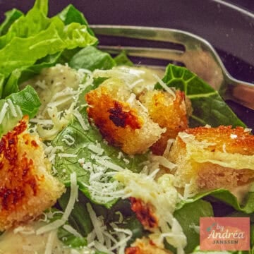Close-up of Caesar salad with crispy golden brown croutons, grated Parmesan cheese, and creamy Caesar dressing on fresh romaine lettuce, with a fork in the background.