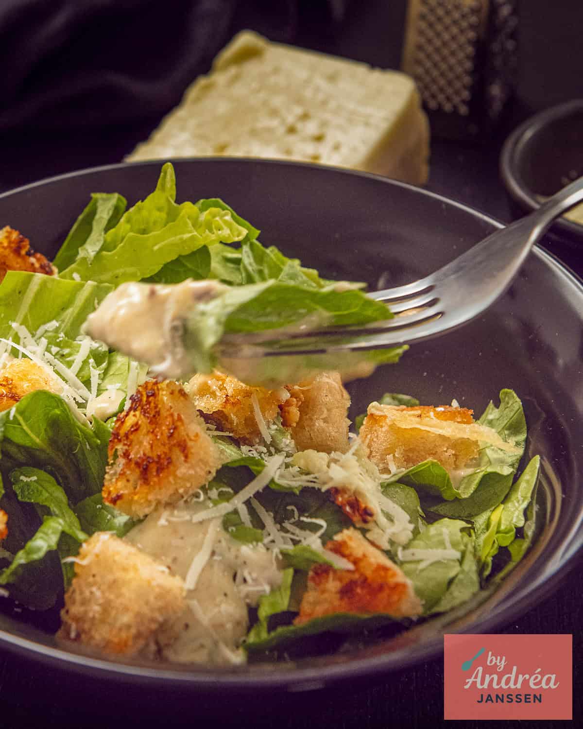 A fork takes a scoop of the Caesar salad with croutons, cheese, and dressing.
