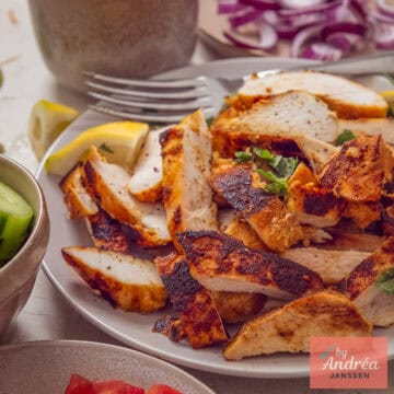A square photo with chicken shawarma on a plate, with some toppings around it.