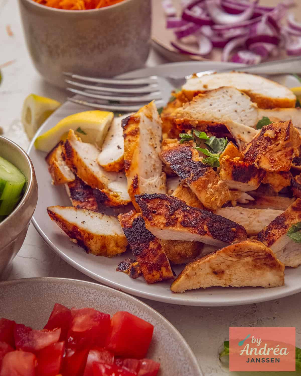 A plate with a mound of chicken shawarma on it. Around it, some toppings for the sandwich.