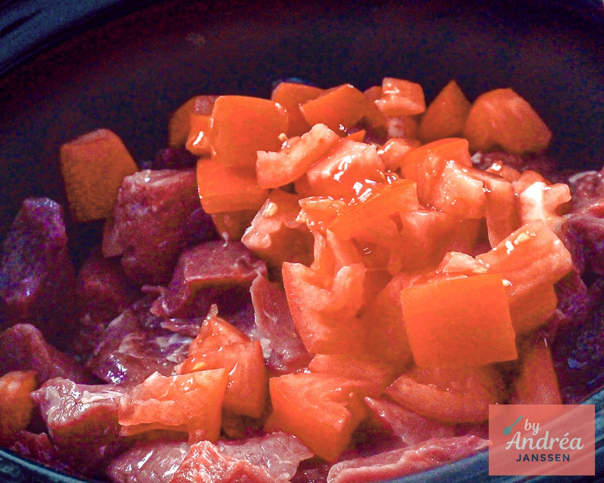 Cubed beef with onion, garlic, and tomato in a slow cooker