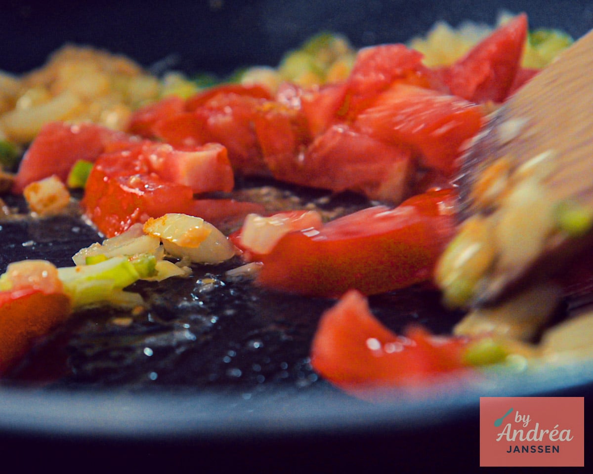 Chopped tomatoes and onion being stirred with a wooden spatula in a skillet for dal.
