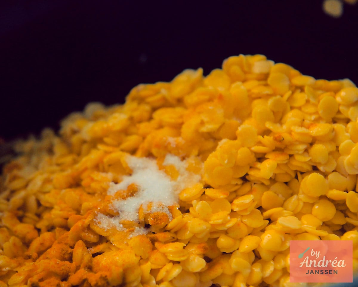 Uncooked yellow split peas topped with turmeric and salt in the slow cooker for dal.