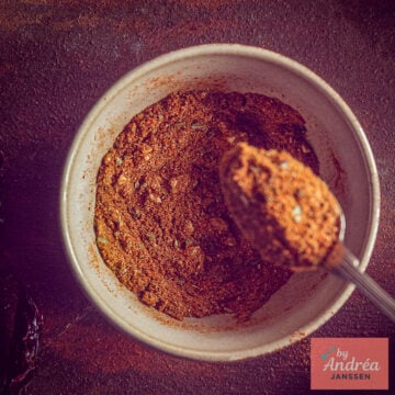 Overhead view of a bowl filled with reddish-brown chili con carne seasoning and a spoonful of the spice mix.