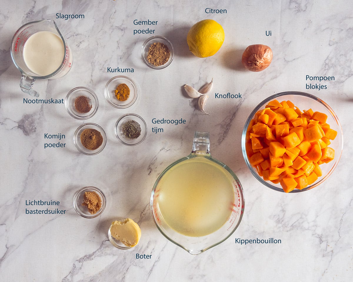 Ingrediënten voor romige pompoensoep uit de slowcooker op een marmeren ondergrond, met Nederlandse labels.