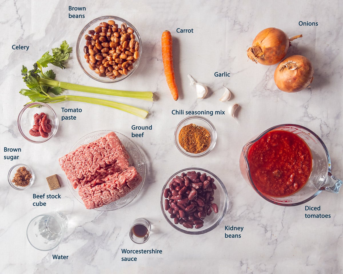 A complete overview of the ingredients for slow cooker chili with ground beef, two kinds of beans, tomatoes, vegetables, and seasonings.