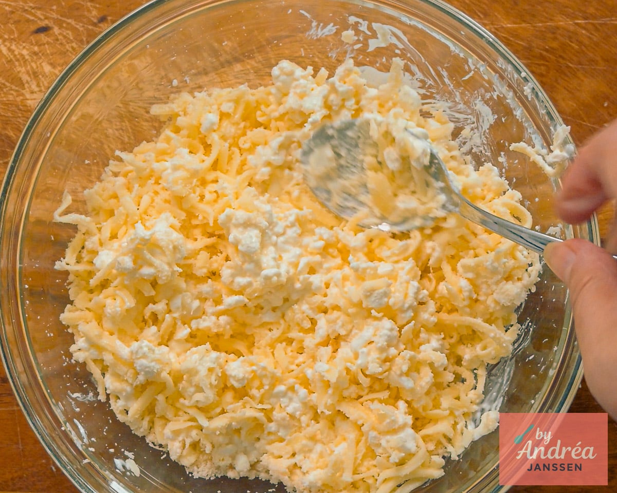 Cottage cheese and shredded cheese being mixed with a spoon in a glass bowl.