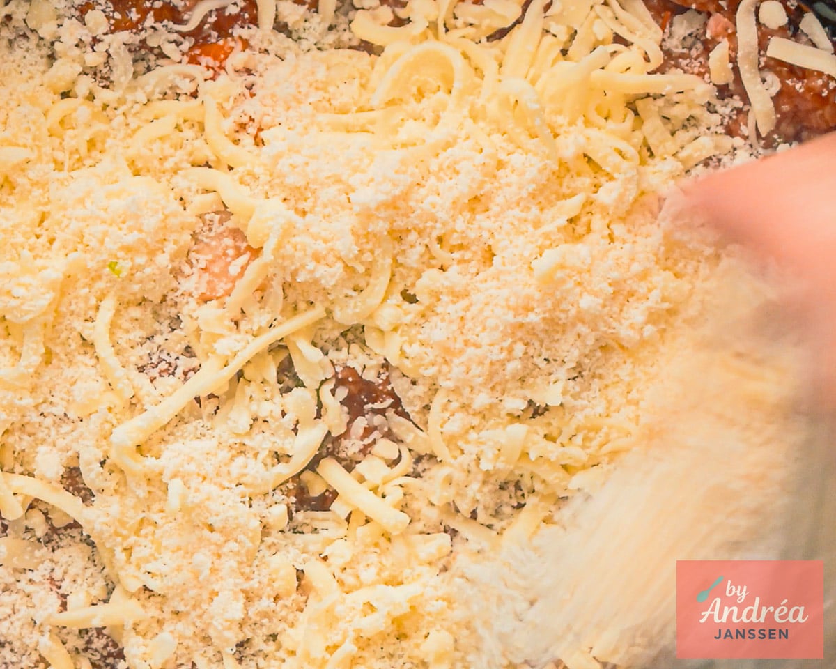 Shredded mozzarella and grated Parmesan being sprinkled over lasagna in the slow cooker.