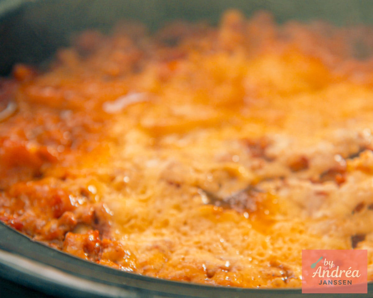 Close-up of lasagna in a slow cooker with melted cheese and tomato meat sauce.