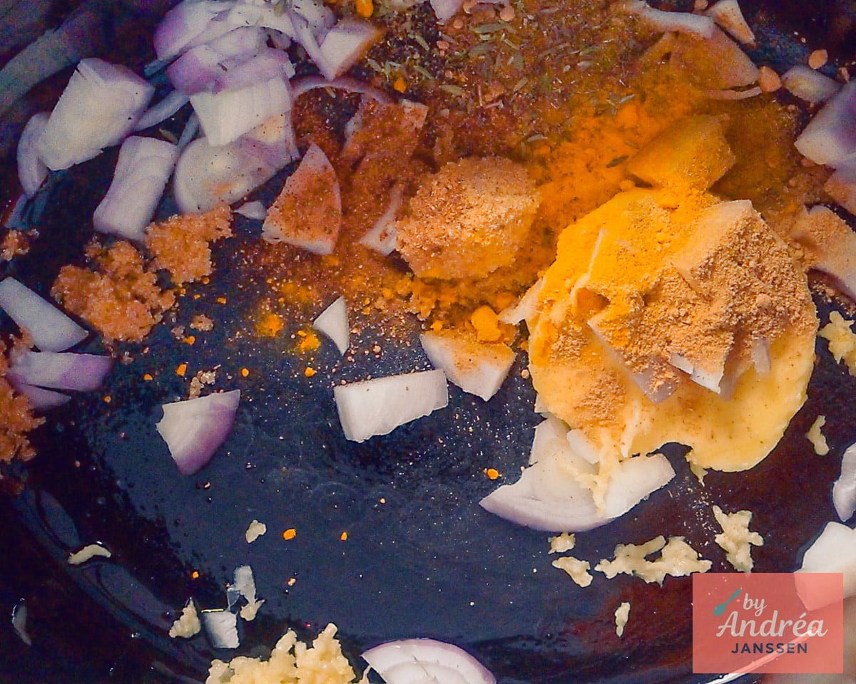 Chopped onion and garlic with butter, brown sugar, and spices in the bottom of the slow cooker.