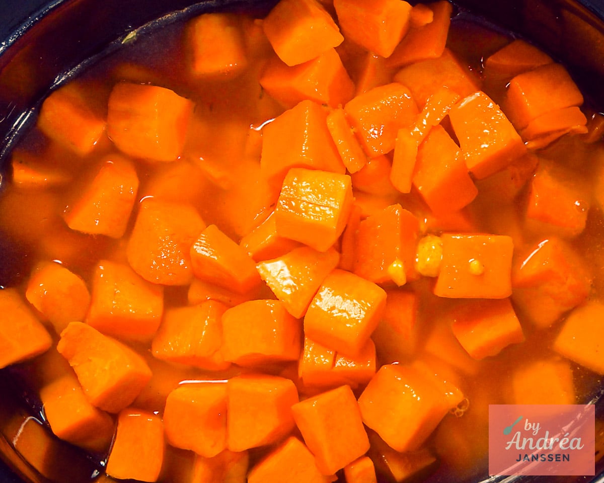 Cubed butternut squash in stock in the uncovered slow cooker, viewed from above.