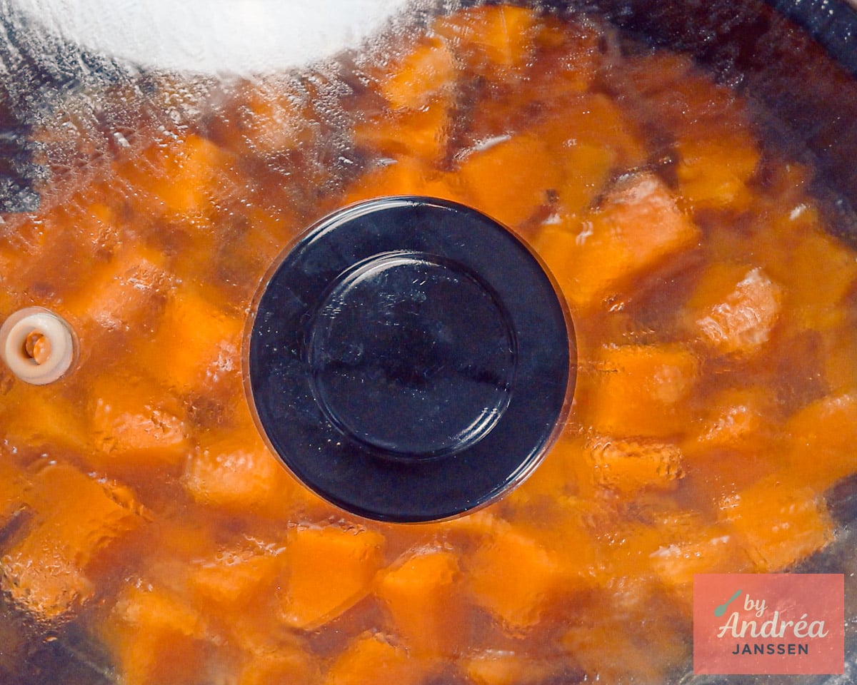 Butternut squash chunks in the slow cooker beneath a glass lid covered with condensation.