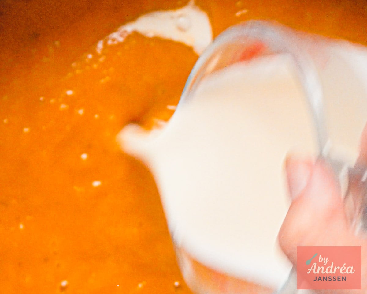 Cream being poured from a glass pitcher into the blended butternut squash soup.