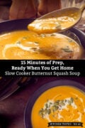 Dark blue bowl of creamy orange butternut squash soup made in a slow cooker, swirled with heavy cream and topped with pumpkin seeds and cracked black pepper. A spoonful is lifted above the bowl, with the slow cooker beside it