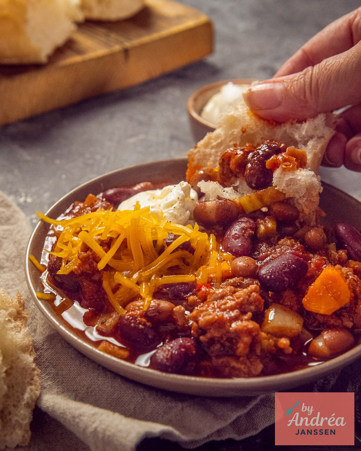 Slow cooker chili con carne with cheddar, sour cream, and bread.