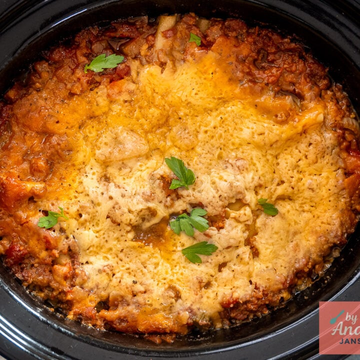 Overhead view of lasagna in a slow cooker with melted cheese, tomato sauce around the edges, and parsley.