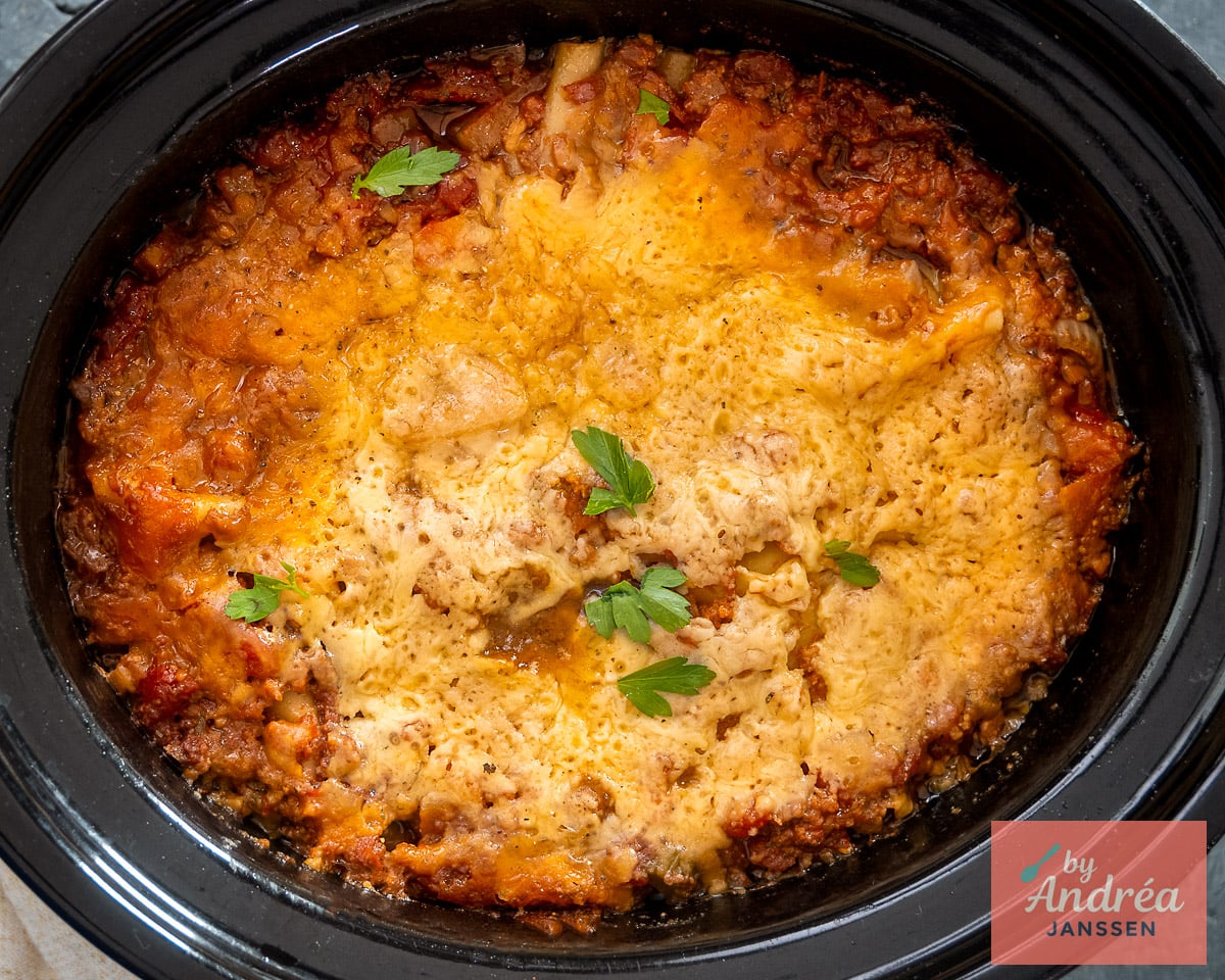 Overhead view of lasagna in a slow cooker with melted cheese, tomato sauce around the edges, and parsley.
