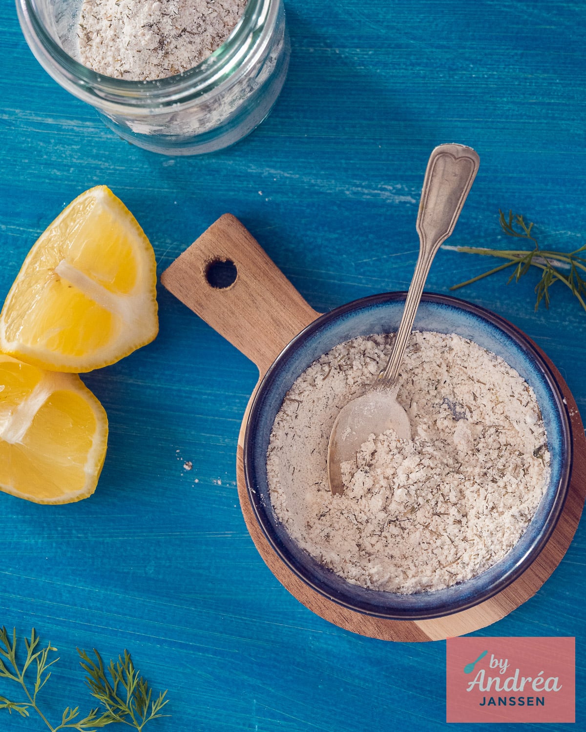 Homemade Dutch fish seasoning in a blue bowl with lemon, dill, and a storage jar