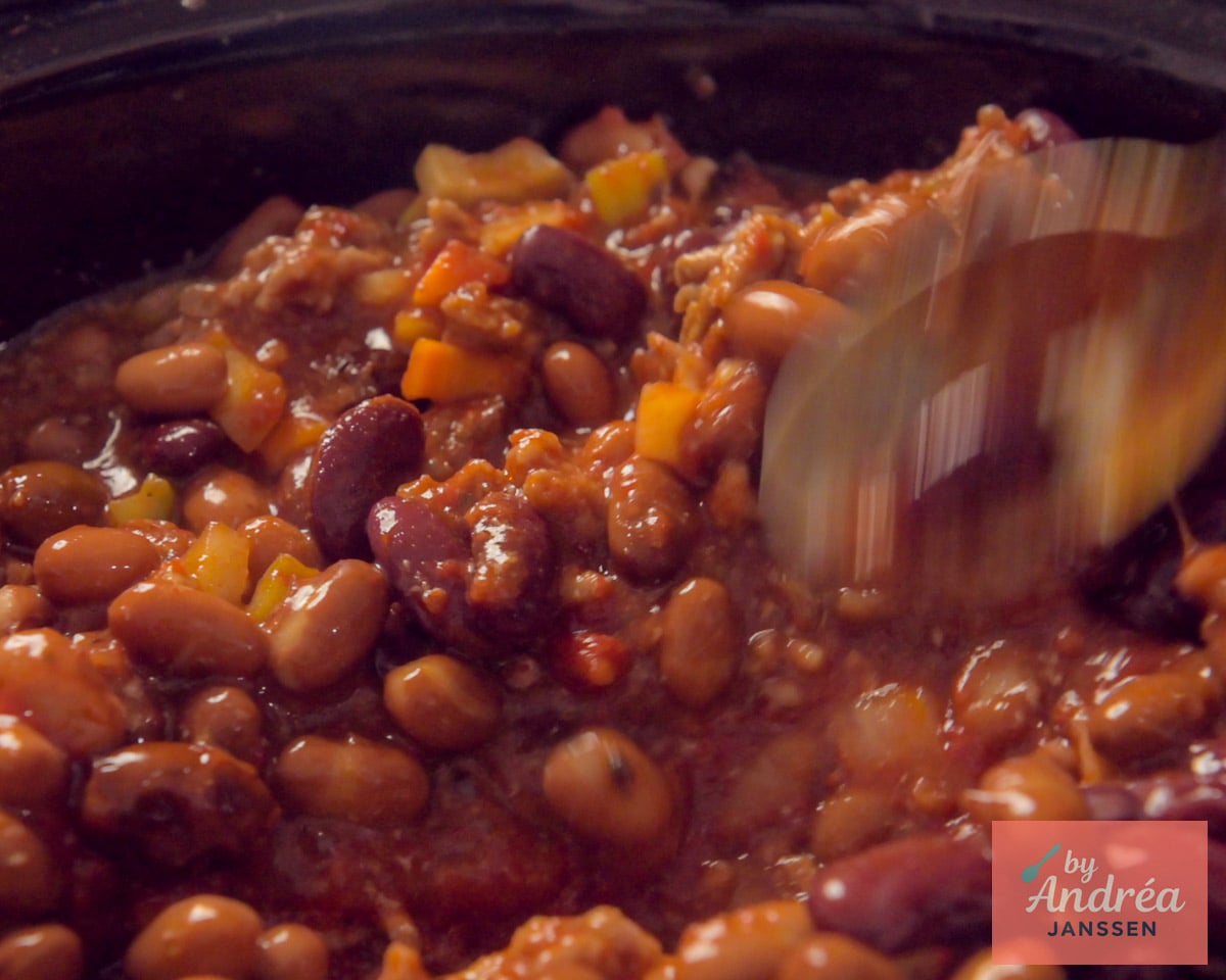 Chili con carne with ground beef and beans being stirred in a slow cooker.