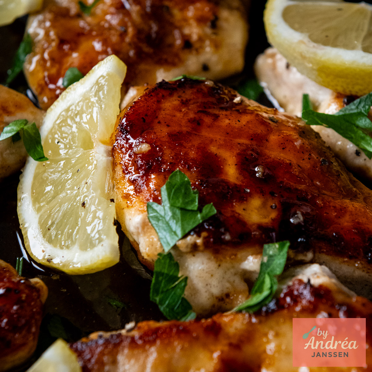 Close-up of golden-brown chicken breast with glossy honey lemon sauce, a lemon slice, and parsley.