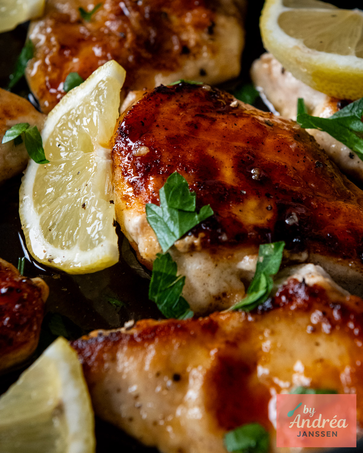 Close-up of chicken breasts coated in glossy honey lemon sauce and garnished with lemon slices and parsley.