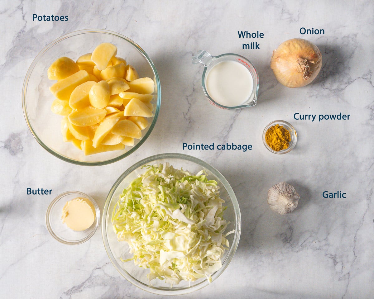Overhead view of potatoes, shredded pointed cabbage, whole milk, onion, curry powder, butter, and garlic with English labels.