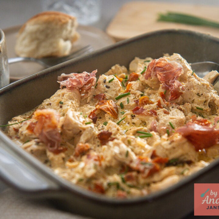 Chicken in creamy Boursin sauce with sun-dried tomatoes, crispy prosciutto, and chives in a gray serving dish.