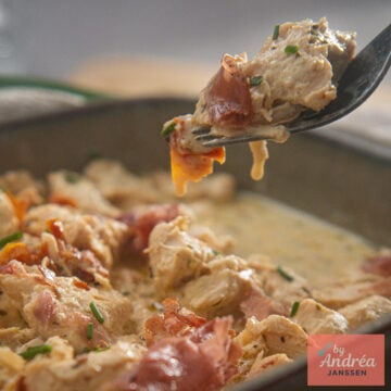 Close-up of a fork holding chicken, creamy Boursin sauce, and crispy prosciutto, with the serving dish in the background.