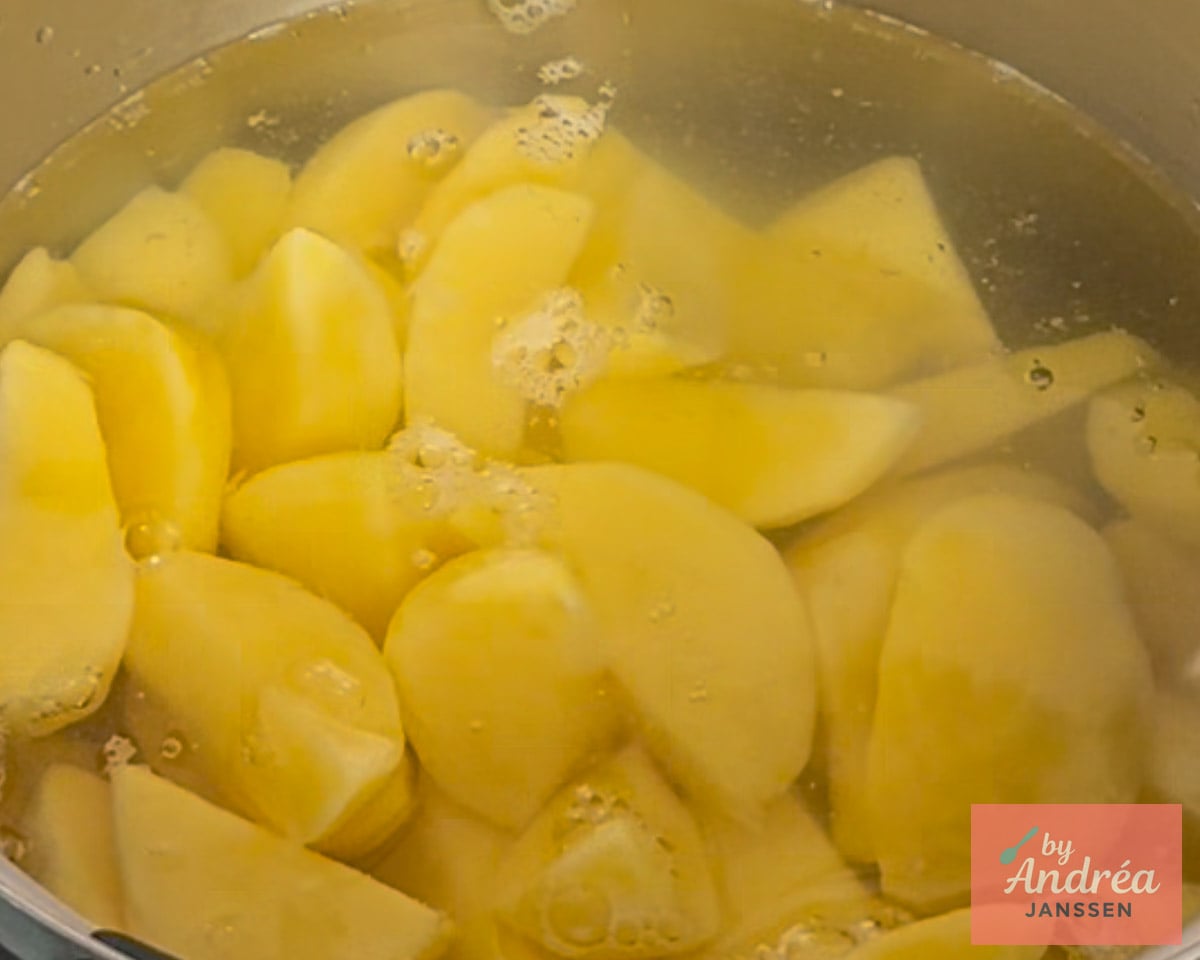 Peeled potato chunks in a pot of water with small bubbles on the surface.