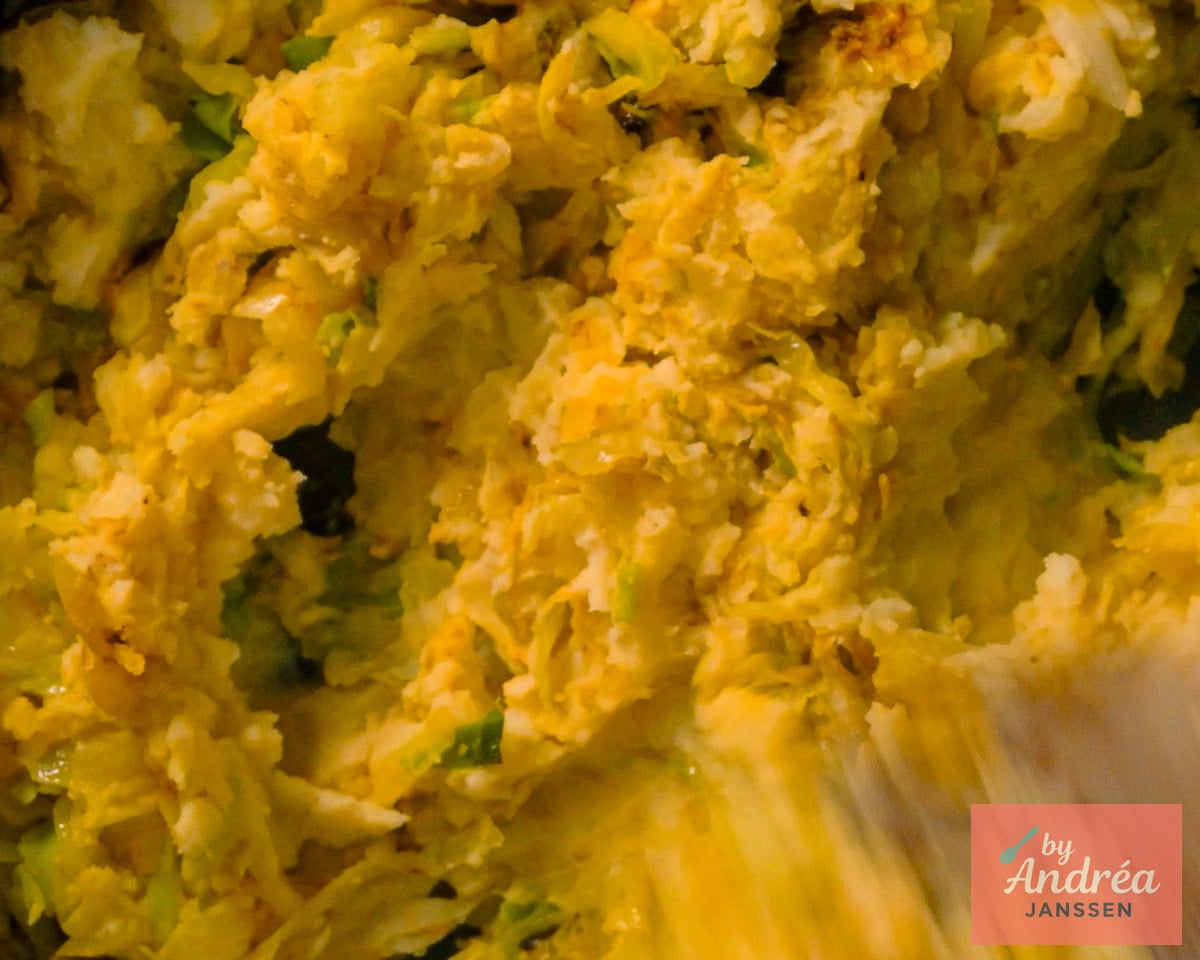 Mashed potatoes being mixed with sautéed cabbage and curry powder in a pan to make a chunky mash.