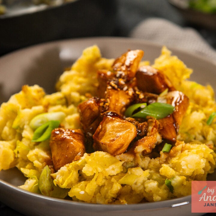 Gray plate of yellow curried cabbage mashed potatoes topped with glossy sweet soy chicken, green onions, and sesame seeds.